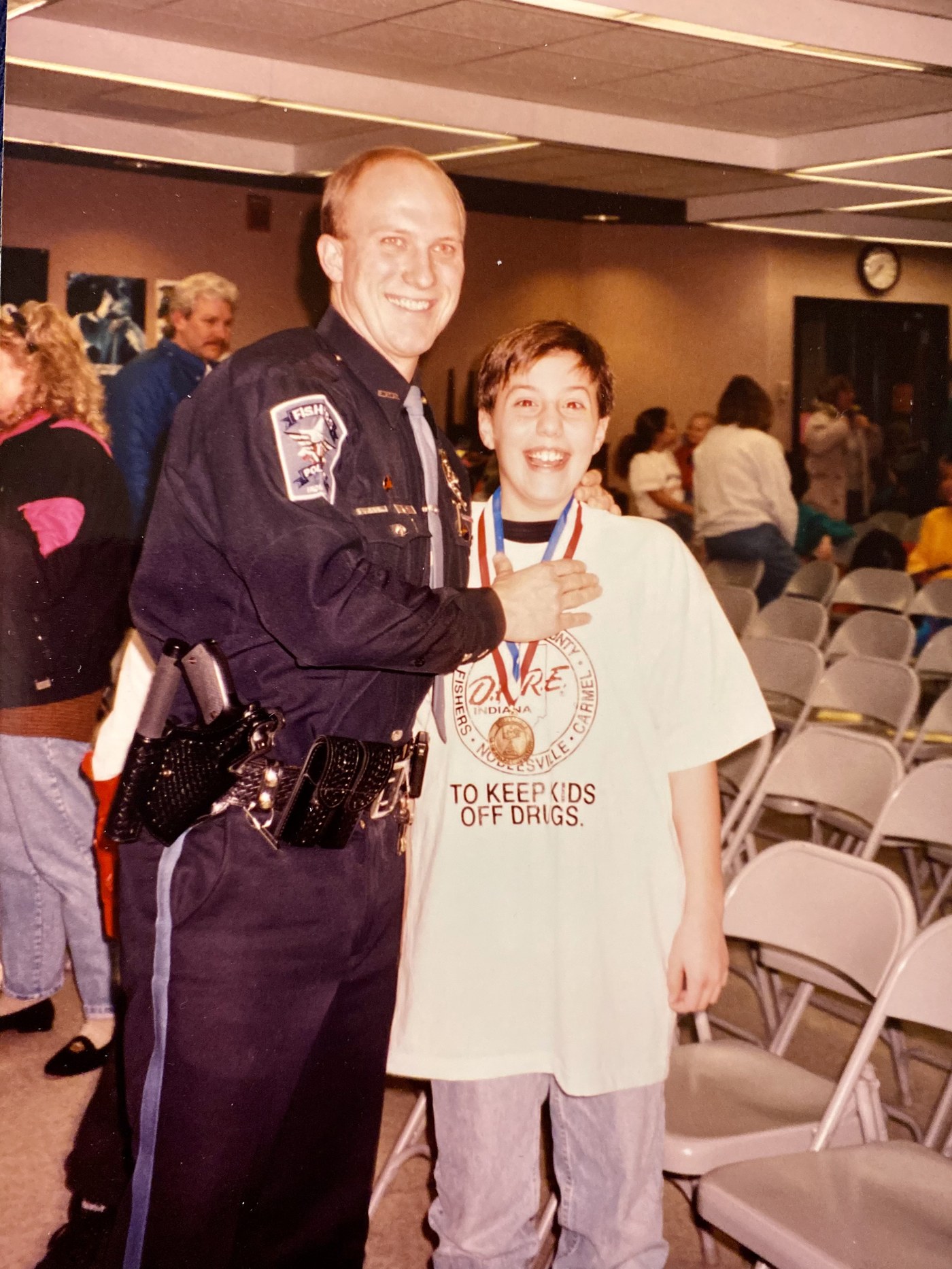 Kevin DeLury as a fifth grader, wearing a D.A.R.E. medal and a shirt reading TO KEEP KIDS OFF DRUGS, beside a Fishers, Indiana police officer